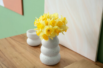 Vase with narcissus flowers and decor on dresser near green wall in living room, closeup