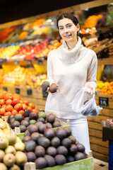 Young woman buyer choosing fresh avocados in vegetable shop