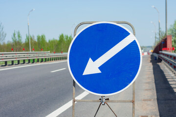 A blue arrow road sign with a downward direction stands on a highway, guiding traffic under a clear...