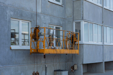 Yellow suspended platform hangs on a building facade, equipped for construction or maintenance...