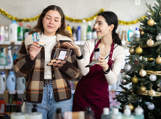 In X mas atmosphere, girl consultant helps female buyer eye shadow set, answers questions and accompanies during shopping, recommended some item. .