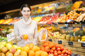 Adult woman buyer choosing fresh oranges in vegetable shop