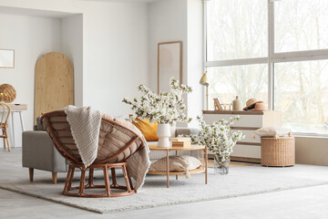 Interior of light living room with sofa, armchair and flowering branches in vases