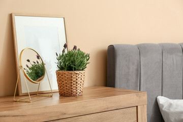 Pot with lavender, photo frame and mirror on dresser near beige wall at home