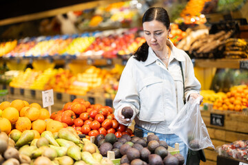 Selective middle-aged female buyer purchasing avocado in grocery store with large assortment
