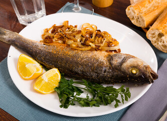 Plate of tasty fish dish - baked sea bass served with fried onion and lemon
