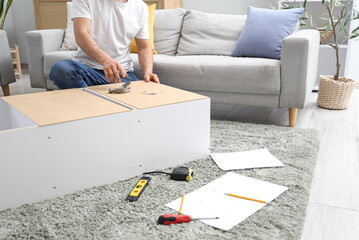 Young man assembling shelf unit on carpet at home