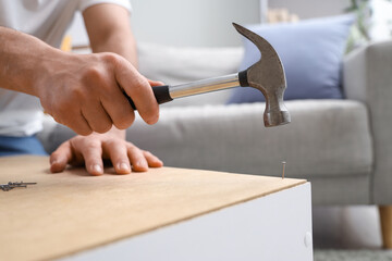Young man with hammer assembling shelf unit at home, closeup