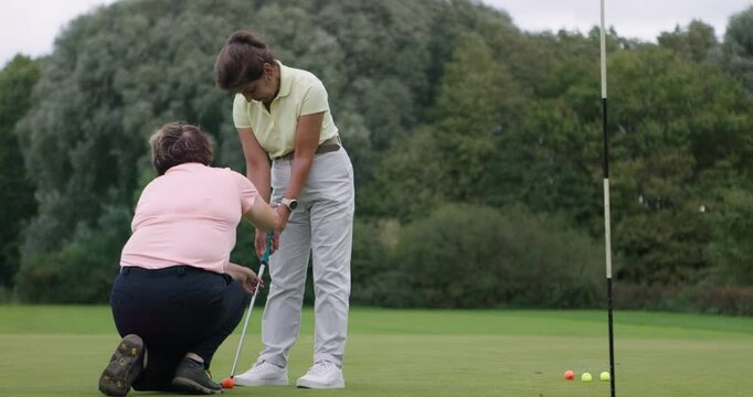 Golf course training, teaching woman and club at field, nature or outdoor help in lesson. Golfing, instructor and person learning to hold putter, grip or form, conversation and healthy exercise sport