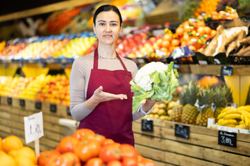 Female grocery store worker offers ripe broccoli cabbage in grocery department of the supermarket