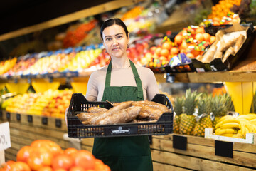 Female salesperson carefully places ripe yucca root on the counter of a grocery supermarket