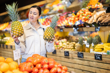 Positive woman choosing ripe pineapples in the produce section of a supermarket