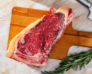 Raw juicy beef entrecote with fresh rosemary ready for cooking on wooden table