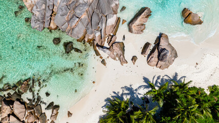 Aerial view of a pristine white sandy beach with large rocks and turquoise waters. Anse Cocos beach, Seychelles.