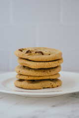 Stack of chocolate chip cookies on a white plate in a well lit kitchen, domestic life concept 