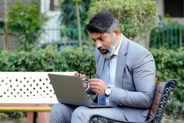 Indian shocked, Worried business man or corporate man feeling tensed while using laptop outdoor at park