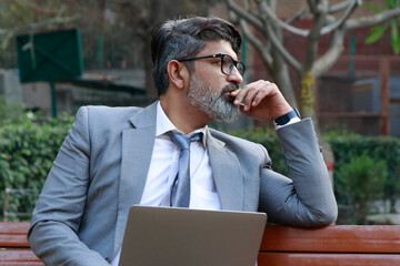 Indian Worried business man or corporate man feeling tensed while using laptop outdoor at park