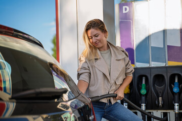 Beautiful woman refueling her car by herself, holding the nozzle and smiling  