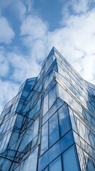Obraz premium Modern architecture with glass facade reflecting blue sky and white clouds
