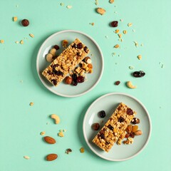 グルテンフリーのグラノーラバーが小さな皿に盛られ、ドライフルーツとナッツが散りばめられた美味しい一品、ミントグリーン背景でシンプルに引き立つ

