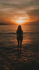 Fototapeta premium Silhouette of a woman standing on the beach watching a sunset.