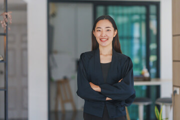 Portrait of a confident asian businesswoman smiling with crossed arms, showcasing professionalism and leadership in a modern office environment