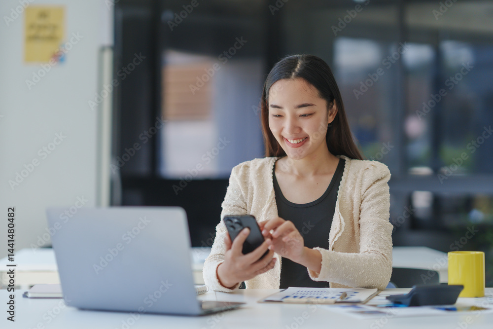 Poster young office worker using mobile phone and smiling while sitting at desk with laptop and documents i
