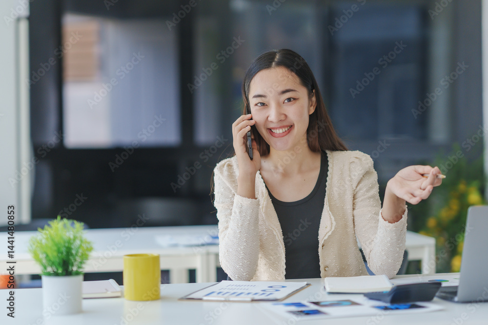 Poster young office worker using smartphone and smiling while sitting at desk and working on laptop compute