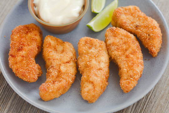 Homemade crispy fried breaded fish sticks or fish fingers made from self-caught triggerfish fillet, served on plate with mayonnaise and lime slices (Selective Focus, Focus in the middle of the image)