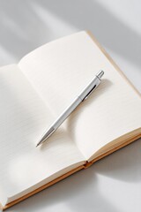 clean notebook open to blank page with single pen lying diagonally on it and gentle shadow falling across