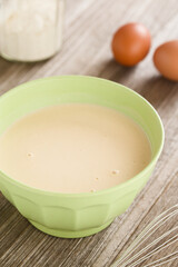 Unleavened batter or dough for crepes, thin french pancakes in bowl with flour and eggs in the back (Selective Focus, Focus on the front of the batter)