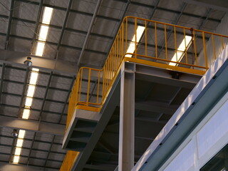 The image depicts an industrial setting with a metal staircase and yellow railings leading to an...