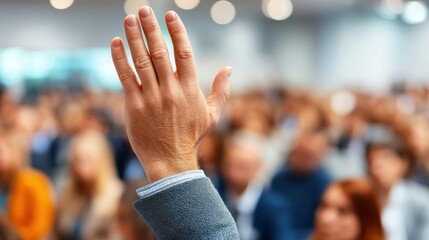 A hand is raised high in a busy event, symbolizing questions or participation.