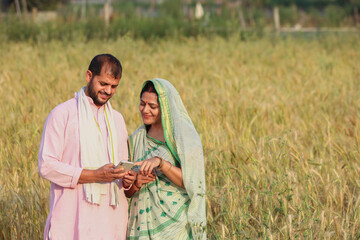 Young indian farmer couple using smart phone at agriculture field together. Rural india.