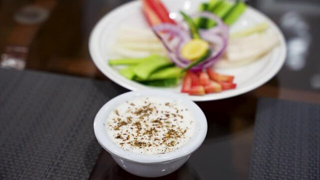 Close-up of spiced yogurt raita served alongside colorful sliced vegetables on a dining table. Pakistan