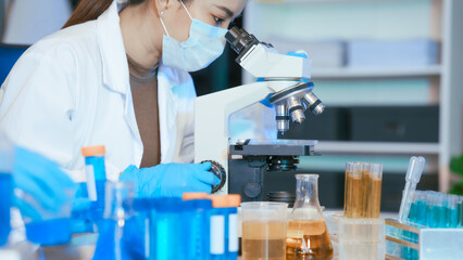 Two Asian female scientists wearing laboratory gloves sit at a table, carefully examining a test...