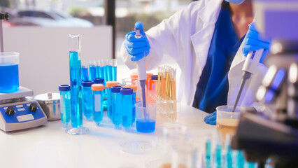 Two Asian female scientists wearing laboratory gloves sit at a table, carefully examining a test...