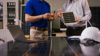 Two Asian businessmen wearing engineer hats table, discussing solar panels and wind turbines. They plan environmental projects, focusing on solar energy solutions and renewable energy installations