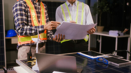 Two Asian businessmen wearing engineer hats table, discussing solar panels and wind turbines. They...