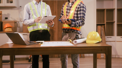 Two male engineers discuss a construction blueprint at a table in a modern office. They focus on architectural design, building structures, roofing,  wall details, planning for a contractor project