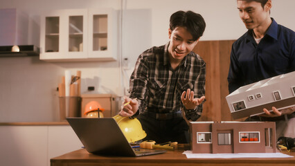Two male engineers review blueprints in an office while discussing model house.They talk about construction projects, architectural design,roof structures,contractor coordination, building materials