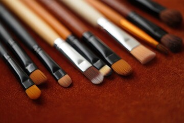 Fototapeta premium Professional Makeup Brushes Laid on Rich Brown Leather — Variety of Sizes, Wooden Handles & Synthetic Bristles in Soft Focus 