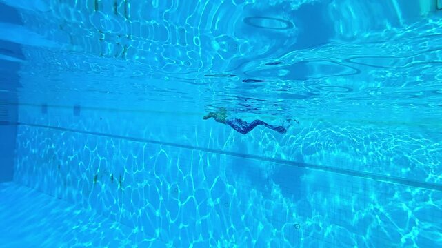 Young woman with mermaid tail swims and dives under sunlit deep water	