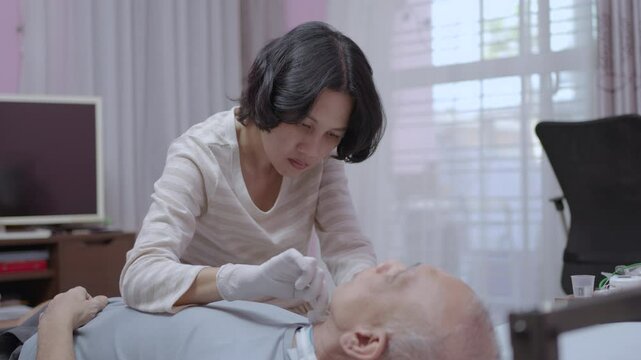 Asian woman uses sterile saline to clean tubes in the neck of a patient undergoing tracheostomy at home.