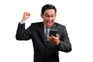 Excited Asian businessman celebrating success with fist raised and looking at smartphone, isolated...