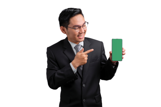 Smiling Asian businessman in suit pointing at smartphone with green screen, isolated on transparent background