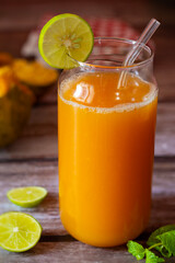 A refreshing glass of bael fruit juice garnished with lime and mint, accompanied by halved bael fruit and lime slices on a rustic wooden table.