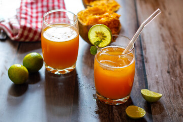 Two glasses of bael juice on a wooden table, garnished with lime and mint, surrounded by fresh...