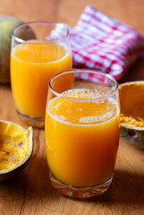 Two glasses of bael juice on a wooden table, garnished with lime and mint, surrounded by fresh limes and split bael fruit in the background.