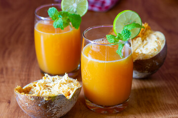 Two glasses of bael juice on a wooden table, garnished with lime and mint, surrounded by fresh...
